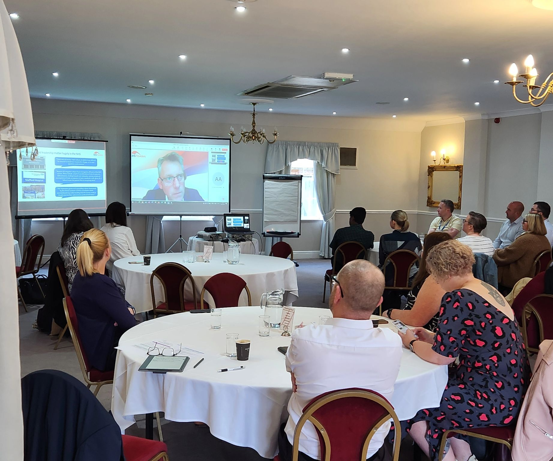 A group of people sat at tables watching a presentation.