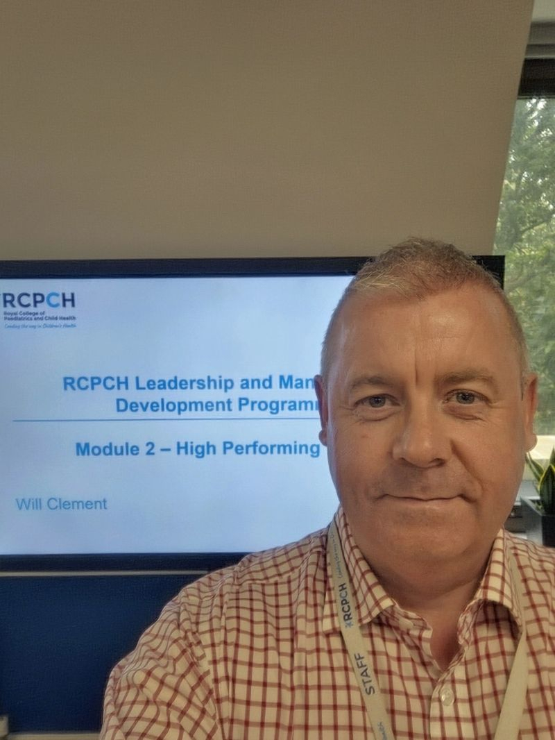 A man stood in front of a presentation screen, which shows a slide of the leadership and management development programme.