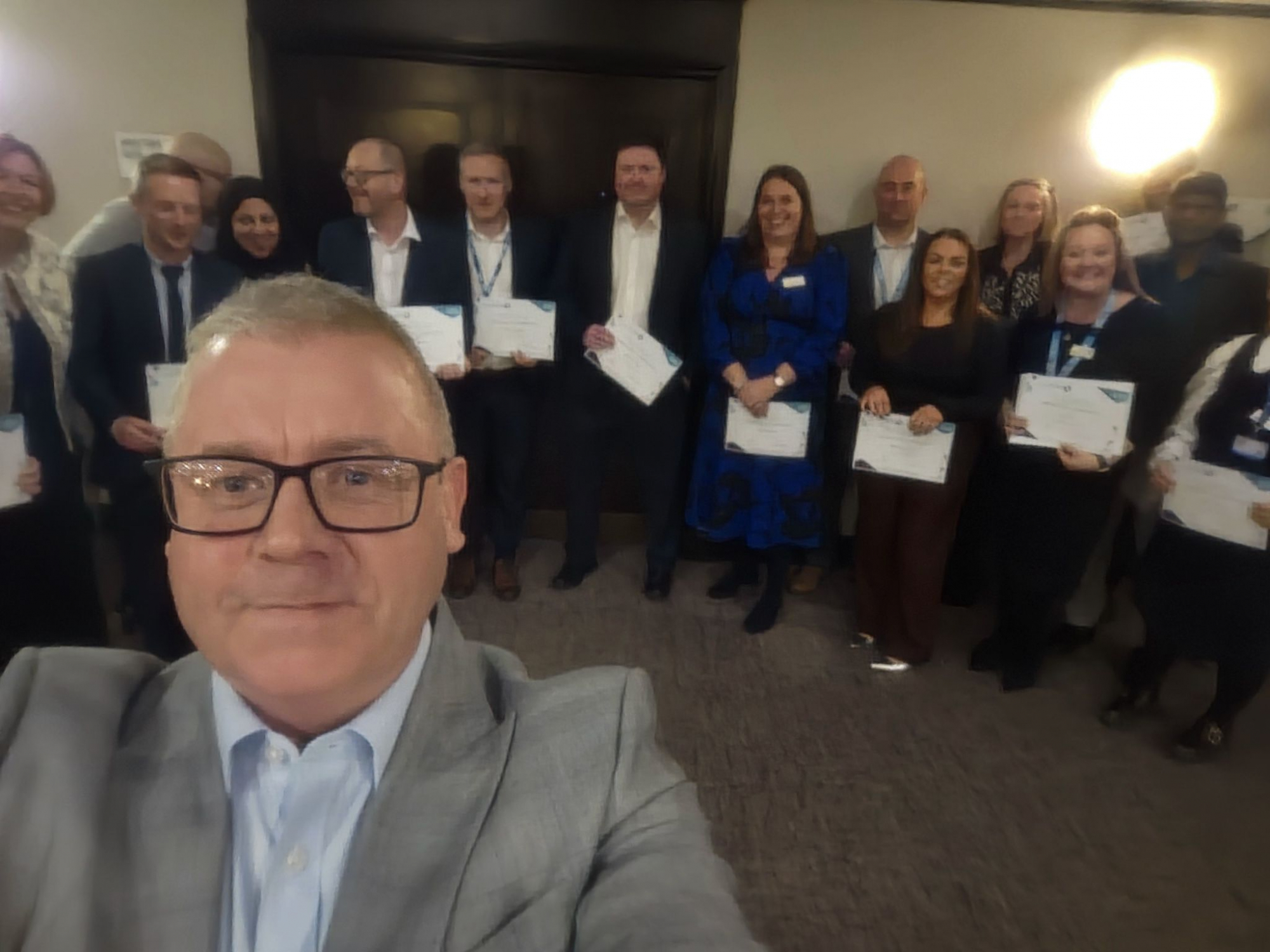 Man stood in front of a large group of people, holding certificates